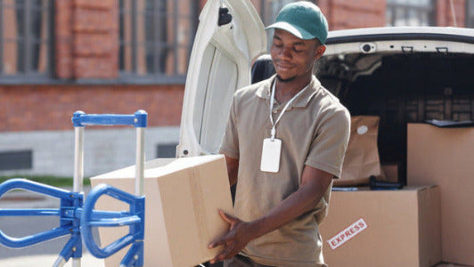 Man unloading boxes from a truck with a cart nearby.