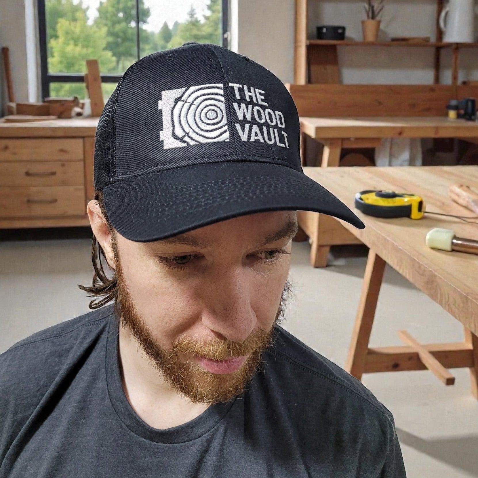 Man wearing a cap with 'The Wood Vault' logo in a workshop setting.