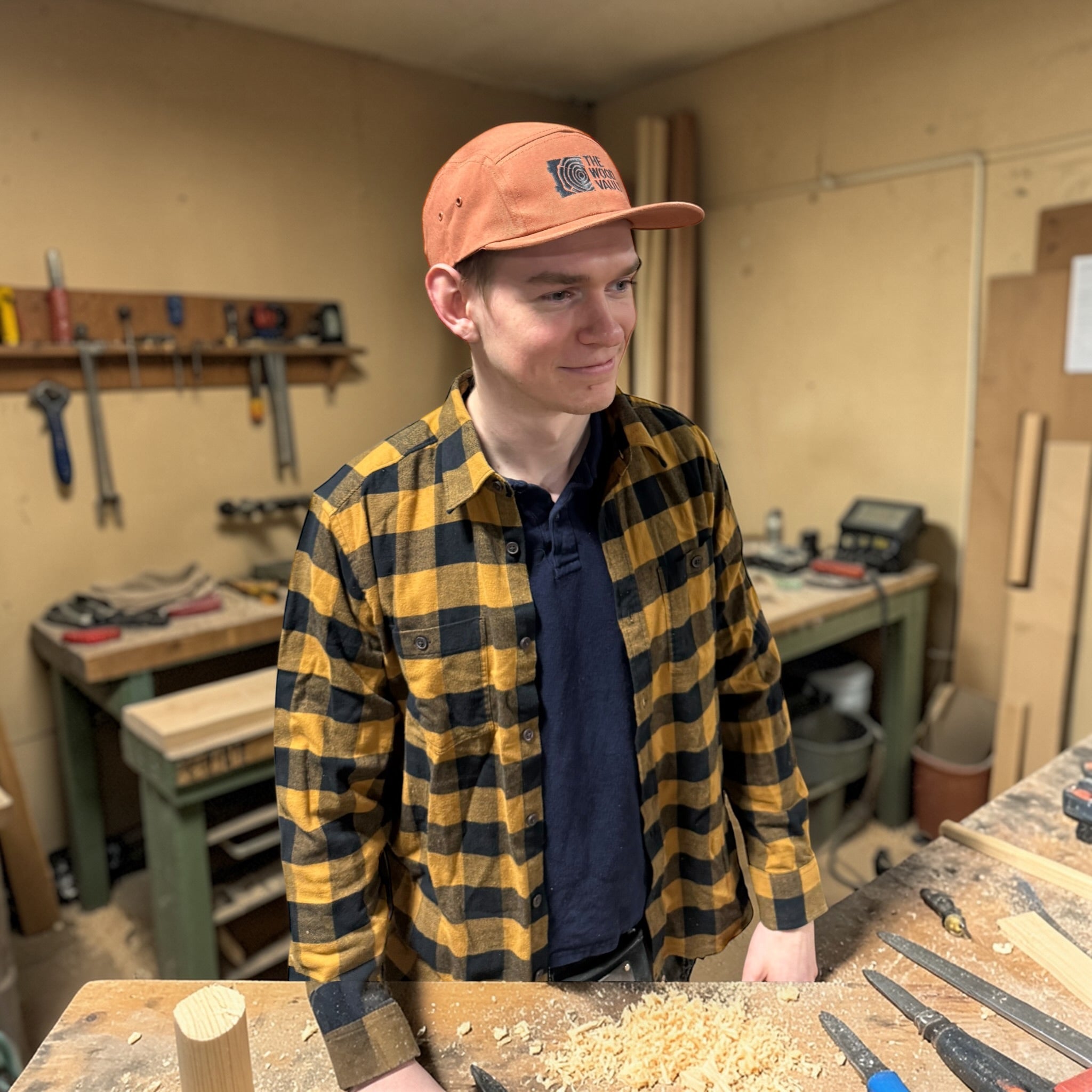 Person wearing a plaid shirt and cap in a workshop setting