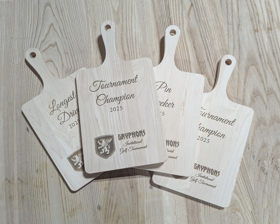 Four wooden cutting boards with engraved text and logos on a wooden surface