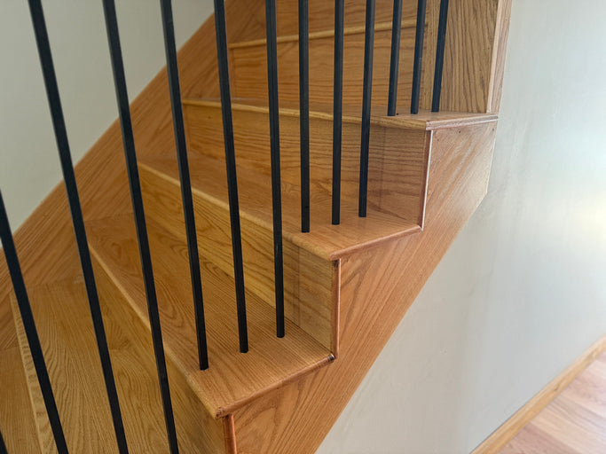 Wooden staircase with black metal balusters against a white wall.