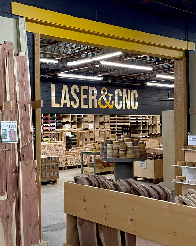 Interior of a warehouse with 'Laser & CNC' branding, wooden planks, and metal components.