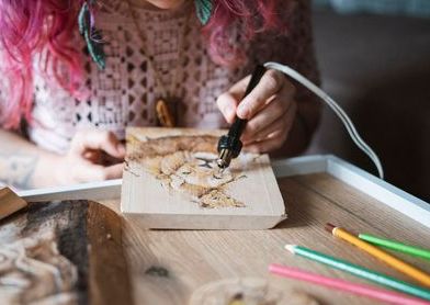 Person working on a craft project with tools and materials on a wooden table.